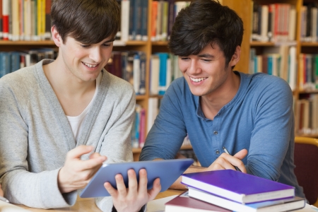 Students sitting at library desk looking at tablet pc in college libraryの写真素材