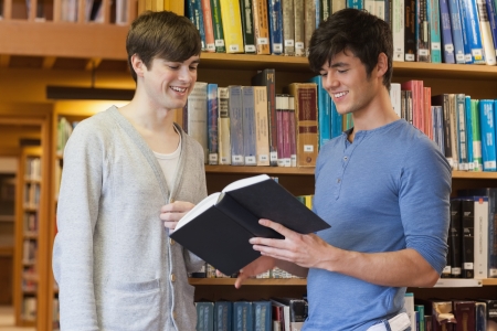 Male students standing in library looking at book in collegeの写真素材