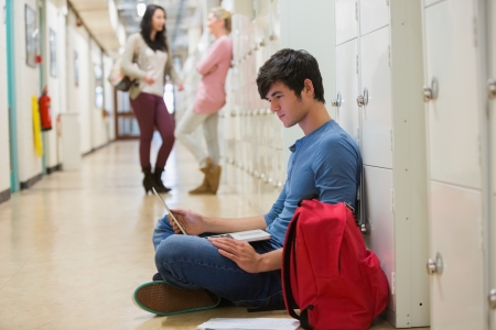 Concentrated student sitting on the floor at the hallway の写真素材