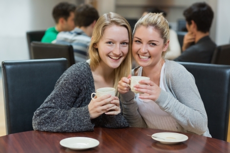 Women sitting at the coffee shop holding cups smiling の写真素材