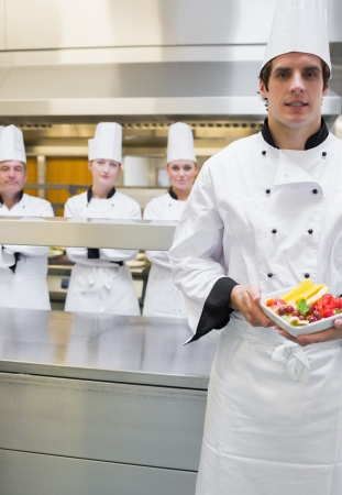 Chef presenting fruit salad with team standing behind himの写真素材
