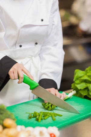 Chef slicing up scallions on chopping board in kitchenの写真素材