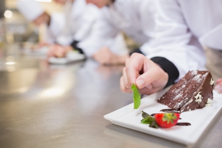 Chocolate cake being garnished by chef in the kitchenの写真素材
