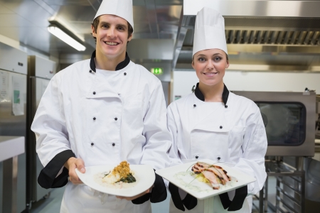 Two smiling Chef's showing plates in the kitchenの写真素材