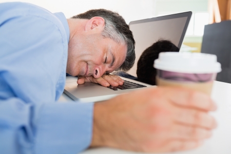 Man holding coffee and sleeping on his laptop on his desk の写真素材