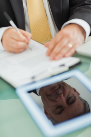 Reflection from a digital tablet screen of a business man writing on a notepad の写真素材