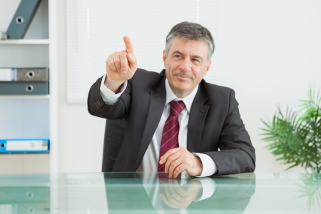 Businessman sitting at his desk pointing at somethingの写真素材