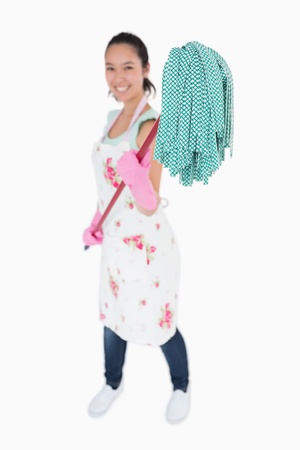 Smiling woman holding a mop in the air with gloves and apron on