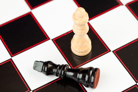 Black chess piece lying with white standing at the chessboard の写真素材