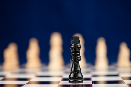 Black chess piece standing at the chessboard white ones behind against blue backgroundの写真素材
