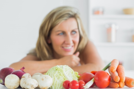 Smiling woman standing behing fresh vegetables in the kitchenの写真素材