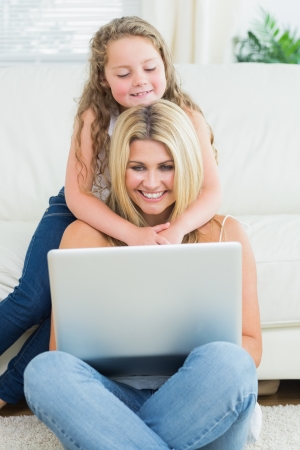 Mother using notebook while sitting on the floor when her daughter hugging her の写真素材