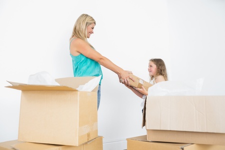 Happy mother and daughter holding moving boxes in empty living roomの写真素材
