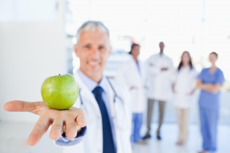 Green apple held by a doctor with a medical team behind himの写真素材