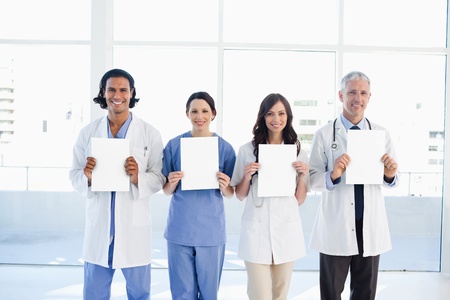 Four smiling medical people standing in front of a window while holding blank sheetsの写真素材