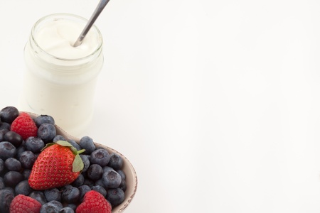 Berries in a heart shaped bowl with white yogurt against a white backgroundの写真素材