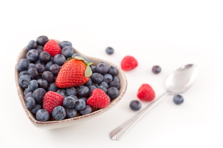 Berries in  a heart shaped bowl  with spoon against a white backgroundの写真素材