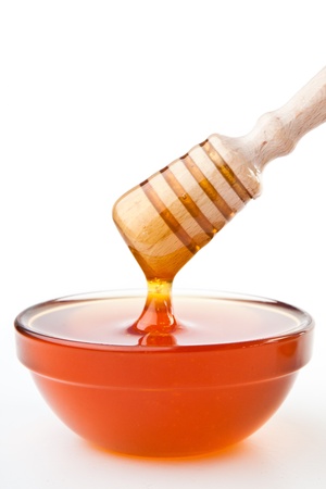 Honey dipper on top of a honey bowl against a white backgroundの写真素材