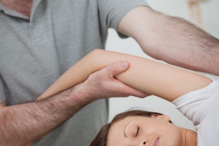 Osteopath holding the arm of a woman while massaging her body in a roomの写真素材