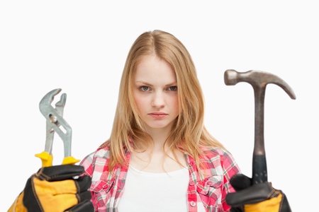 Serious woman holding a hammer and and a wrench against white backgroundの写真素材