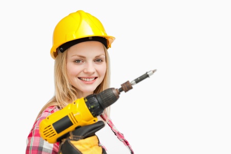 Woman holding an electric screwdriver while smiling against white backgroundの写真素材