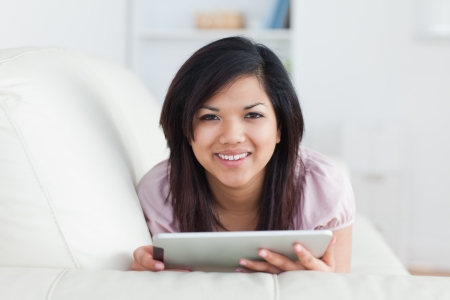 Woman smiling while resting on a couch and playing with a tablet in a living roomの写真素材
