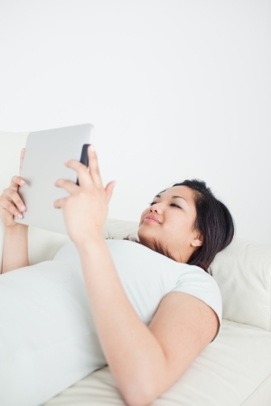 Woman lying on a sofa while holding a tactile tablet in a living roomの写真素材