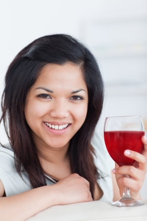 Close-up of a smiling woman holding a glass of red wine in a living roomの写真素材