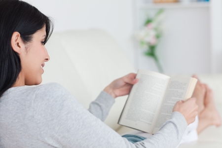 Woman reading a book while laying on a sofa in a living roomの写真素材