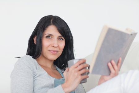 Woman holding a grey mug and a book in a living roomの写真素材