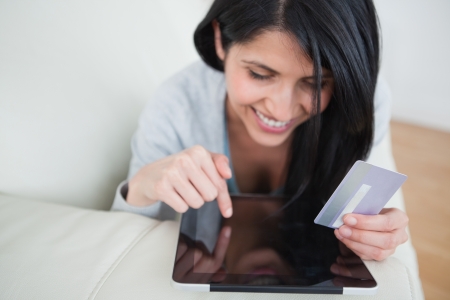 Woman touching a tactile tablet and holding a credit card in a living roomの写真素材