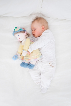 Baby sleeping while embracing a plush doll in a bedroomの写真素材