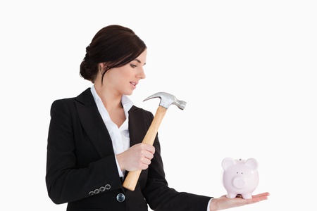 Businesswoman going to break a piggy-bank with a hammer against white backgroundの写真素材
