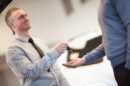 Smiling man giving keys ta a man in a car shopの写真素材