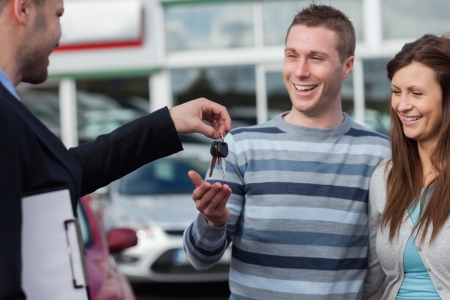 Couple receiving car keys by a dealer in a dealershipの写真素材