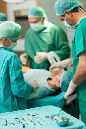 Table full of surgical tools in front of a surgical team working in a surgical roomの写真素材