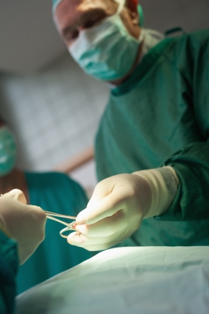 Surgeon taking scissors from a gloved hand in a surgical roomの写真素材