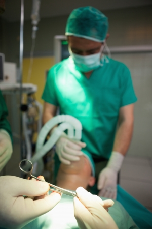 Surgical scissors in gloved hands over a sleeping patient in a surgical roomの写真素材