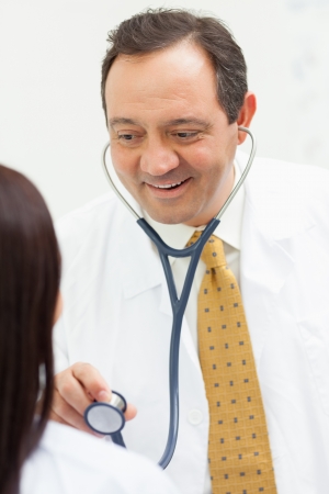 Doctor holding a stethoscope with a patient in an examination roomの写真素材