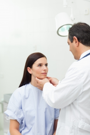 Doctor touching the neck of a patient in an examination roomの写真素材