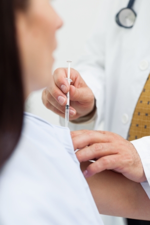 Close up of a doctor doing an injection to a patient in an examination roomの写真素材