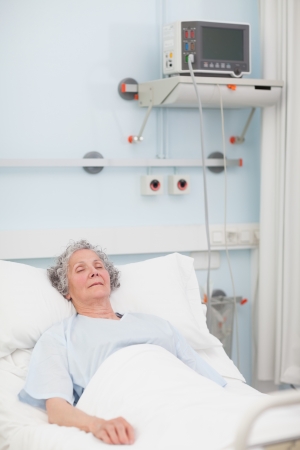 Elderly patient lying with closed eyes in hospital wardの写真素材