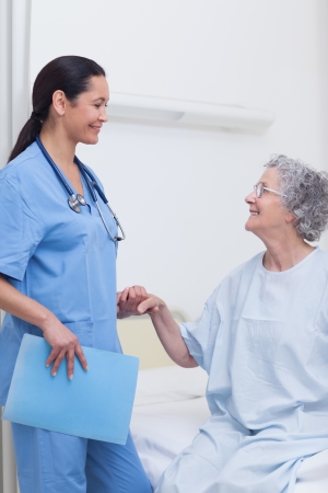 Elderly patient holding the hand of a nurse in hospital wardの写真素材