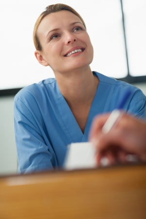 Nurse looking at someone who signing a paper in the hospital receptionの写真素材