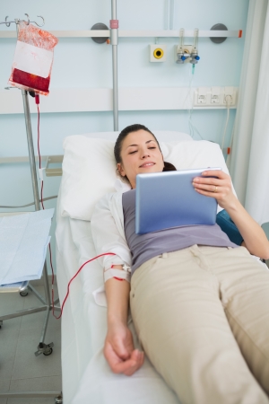 Female transfused patient holding a tablet computer in hospital wardの写真素材