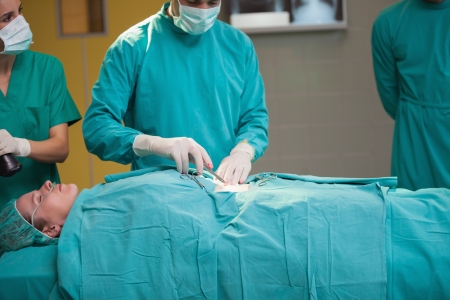 Surgeon opening the belly of a patient in operating theaterの写真素材
