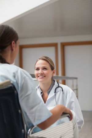 Smiling doctor squatting next to a patient on a wheelchair in hospital corridorの写真素材