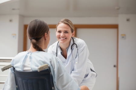 Smiling doctor in front of a patient on a wheelchair in hospital hallwayの写真素材