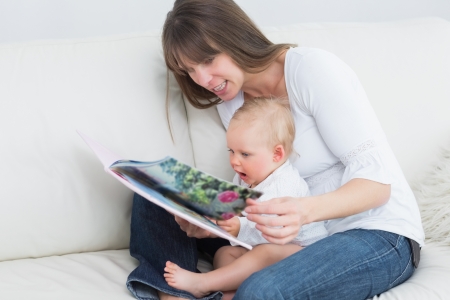 Mother reading a book with a baby in living roomの写真素材