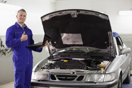 Mechanic holding a computer with thumb up in a garageの写真素材